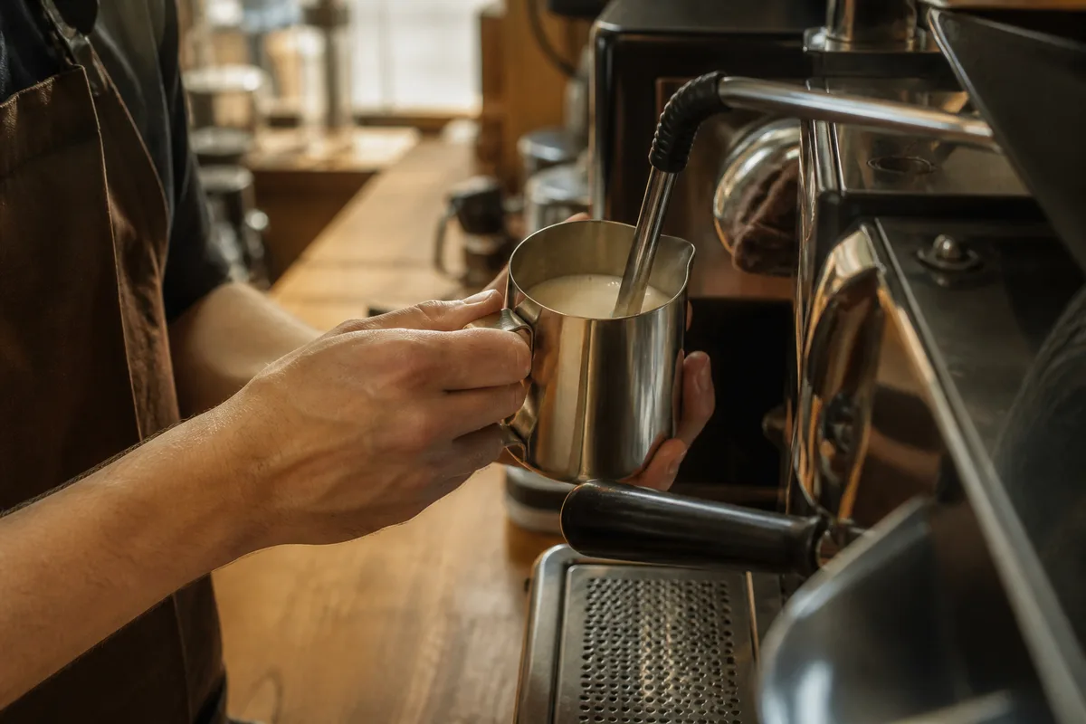 Barista texturant du lait dans un pichet en inox devant une machine à espresso
