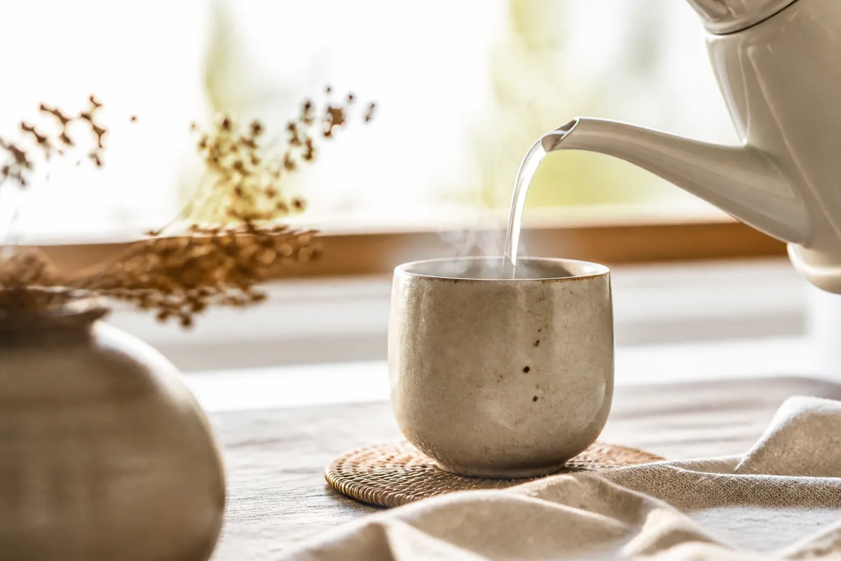Bouilloire versant un filet d&rsquo;eau frémissante dans une tasse en céramique